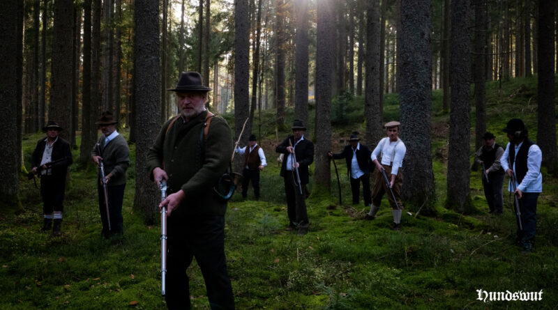Szene aus dem Film mit Männern die mit Gewehren durch einen Wald ziehen