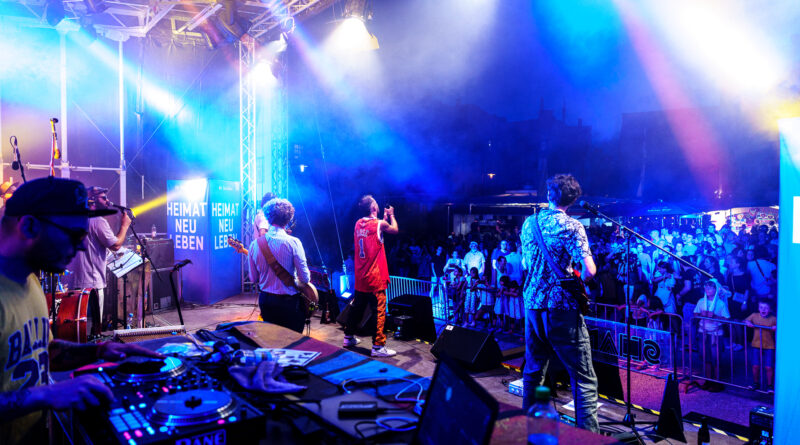Eine Band steht auf einer blau beleuchteten Bühne vor Publikum