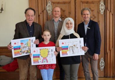 Die Gewinnerinnen des Gestaltungswettbewerbs Rimas und Sophie halten Ihre Entwürfe in die Kamera. Der dritte Bürgermeister Hans-Martin Steiger hält das Motiv der nicht anwesenden Gewinnerin Jule in den Händen. Mit dabei die Verantwortlichen für die Sparkasse Frédéric Voigt und für allgäu mail Timm Schwegler. Alle stehen im Rathaus vor einer alten Holztür.