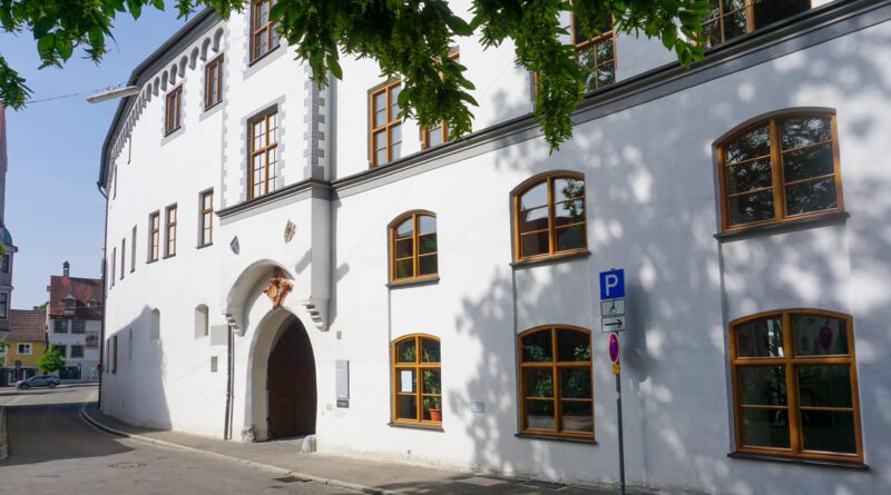 Die Fassade des Antonierhauses in Memmingen an einem sonnigen Tag mit Blättern von Bäumen im Vordergrund