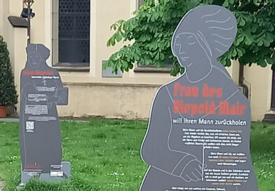 Lebensgroße Stelen, die Umrisse historischer Figuren darstellen auf denen ihre Biografie und geschichtliche Fakten gedruckt sind, stehen auf dem Rasen vor der Martinskirche