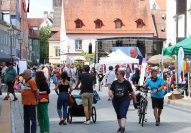 Menschen laufen an einem sonnigen tag über den historischen Weinmarkt und begutachten die aufgebauten Marktstände und die Bühne im Hintergrund