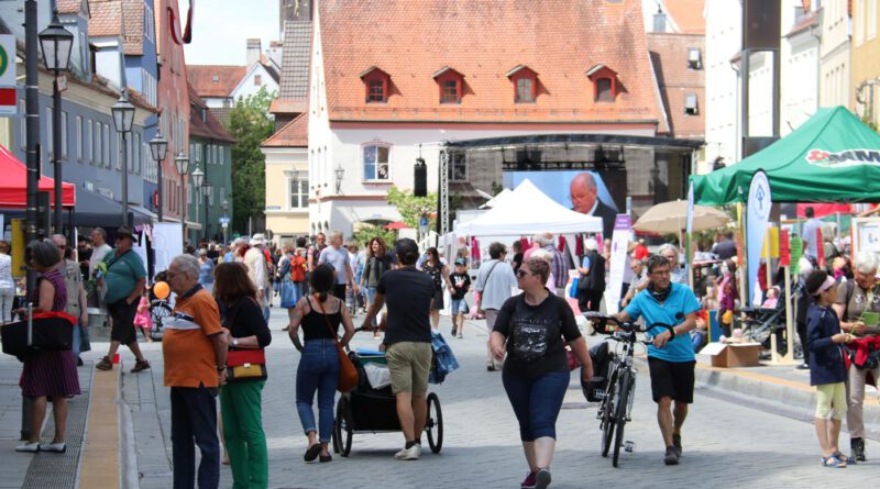 Menschen laufen an einem sonnigen tag über den historischen Weinmarkt und begutachten die aufgebauten Marktstände und die Bühne im Hintergrund