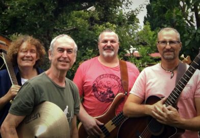 Die Mitglieder der Blue House Rockband mit ihren Instrumenten mit grünen Bäumen und Büschen im Hintergrund