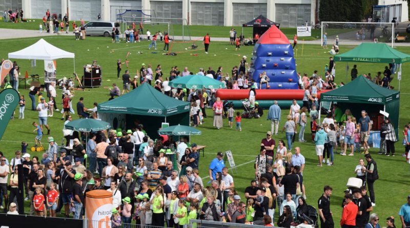 Infostände und Spielstationen auf einem Fußballrasen mit verschiedenen Besuchern