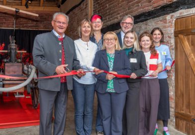 Menschen zerschneiden feierlich ein rotes Band vor einer Ausstellung in einem historischen Gebäude