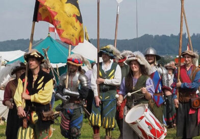 mittelalterlich gekleidete Personen marschieren an Zelten vorbei