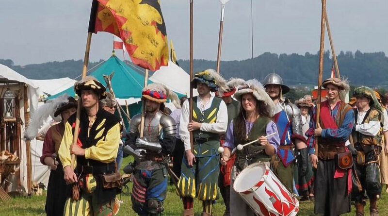 mittelalterlich gekleidete Personen marschieren an Zelten vorbei