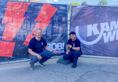 Zwei Mitarbeiter von Radio Bob! und Kaminwerk hocken vor zwei Bannern mit den Logos der beiden Institutionen