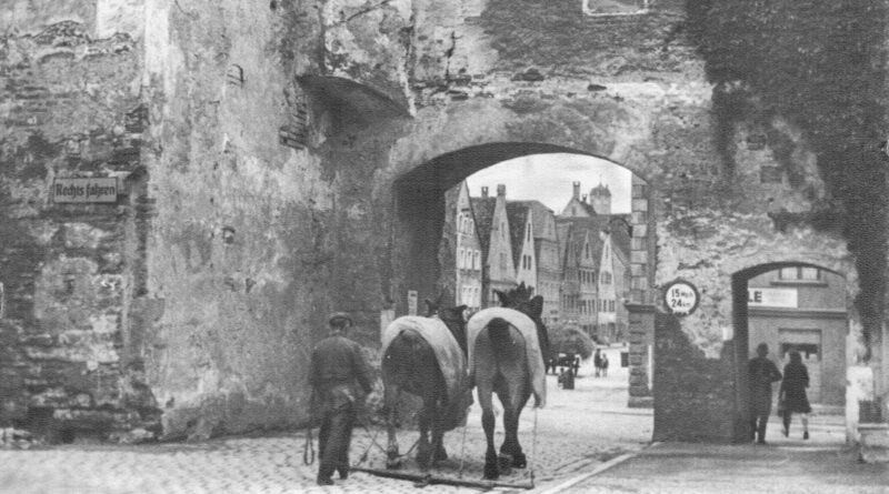 Historisches Schwarz-weiß Foto: ein Mann führt zwei Pferde durch ein Stadttor