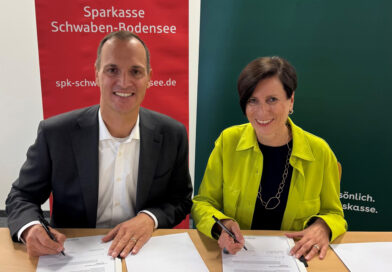 Ein Mann und eine Frau sitzen lächelnd hinter einem Tisch und unterschreiben ein Dokument