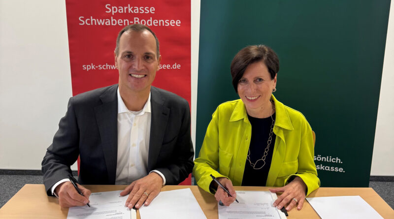 Ein Mann und eine Frau sitzen lächelnd hinter einem Tisch und unterschreiben ein Dokument