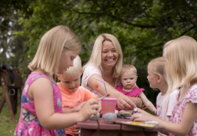 <span style="font-size: 16px;">30. Januar, Memmingen </span><br>Freie Plätze im Qualifizierungskurs für neue Tagesmütter und-väter Eine lachende Frau spielt mit Kindern an einem Tisch in einer Grünanlage