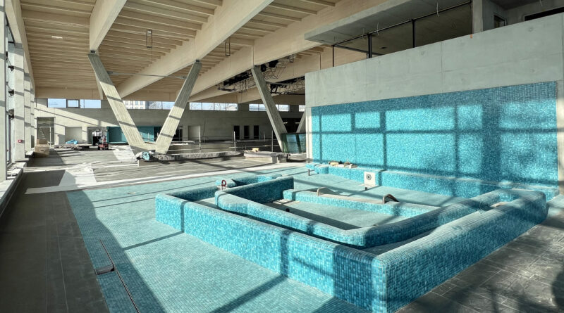 ein blau gefliestes Schwimmbecken in einer Halle, in der noch Bauarbeiten stattfinden.