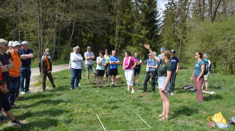 „Keep cool – gesund bleiben in heißen Zeiten“ Auf einer sonnigen Waldlichtung hören mehrere Menschen einem Vortrag zu