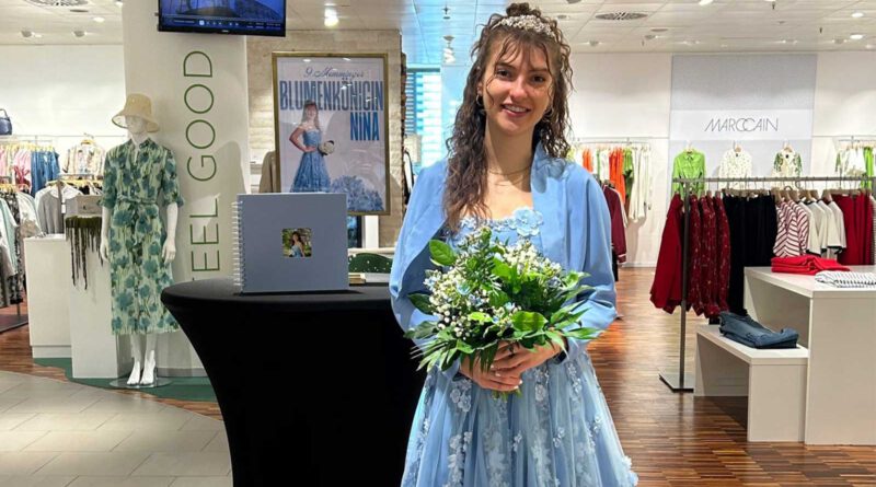 eine lächelnde junge Frau in einem hellblauen Kleid steht mit einem Blumenstrauß in der Hand in einem Modegeschäft
