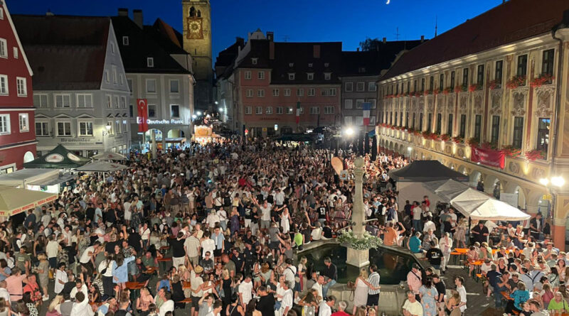 <span style="font-size: 16px;">13. Juni, Memmingen </span><br>Memmingen feiert das traditionelle Stadtfest Menschen feiern in der Dämmerung auf einem Marktplatz