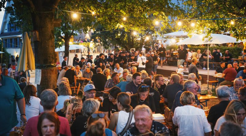 feiernde Menschen in einem gemütlich beleuchtetem Biergarten in der Dämmerung