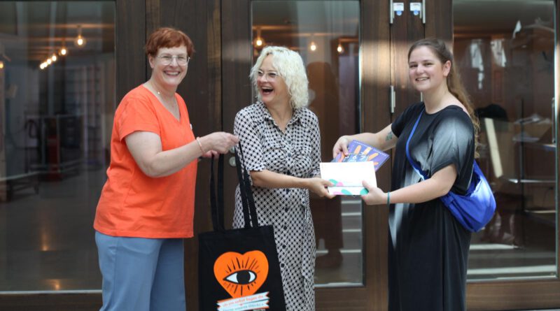 Das Landestheater Schwaben wird Gastgeber der Bayerischen Theatertage 2028 Drei Frauen vor dem Eingang eines Theaters überreichen sich die Spielzeitprogramme des Theaters