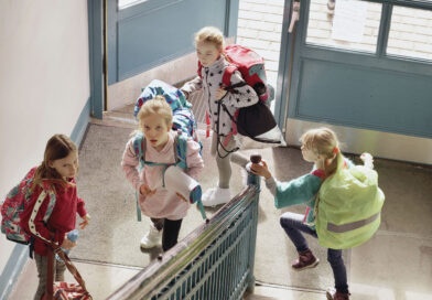 AOK-Aktion „Schulranzen Fit“ für gesunde Kinderrücken Schulkinder mit Schulranzen und Taschen gehen durch ein Treppenhaus in einem Schulgebäude.